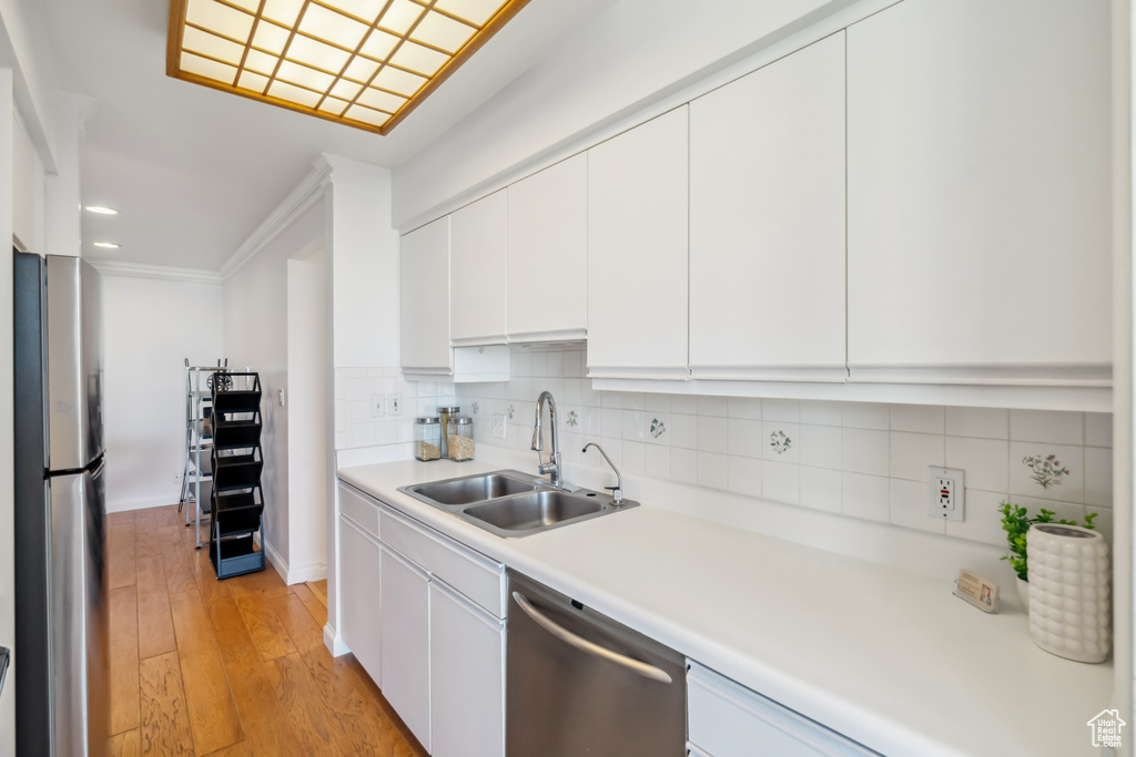 Kitchen featuring appliances with stainless steel finishes, light countertops, light wood finished floors, tasteful backsplash, and white cabinets