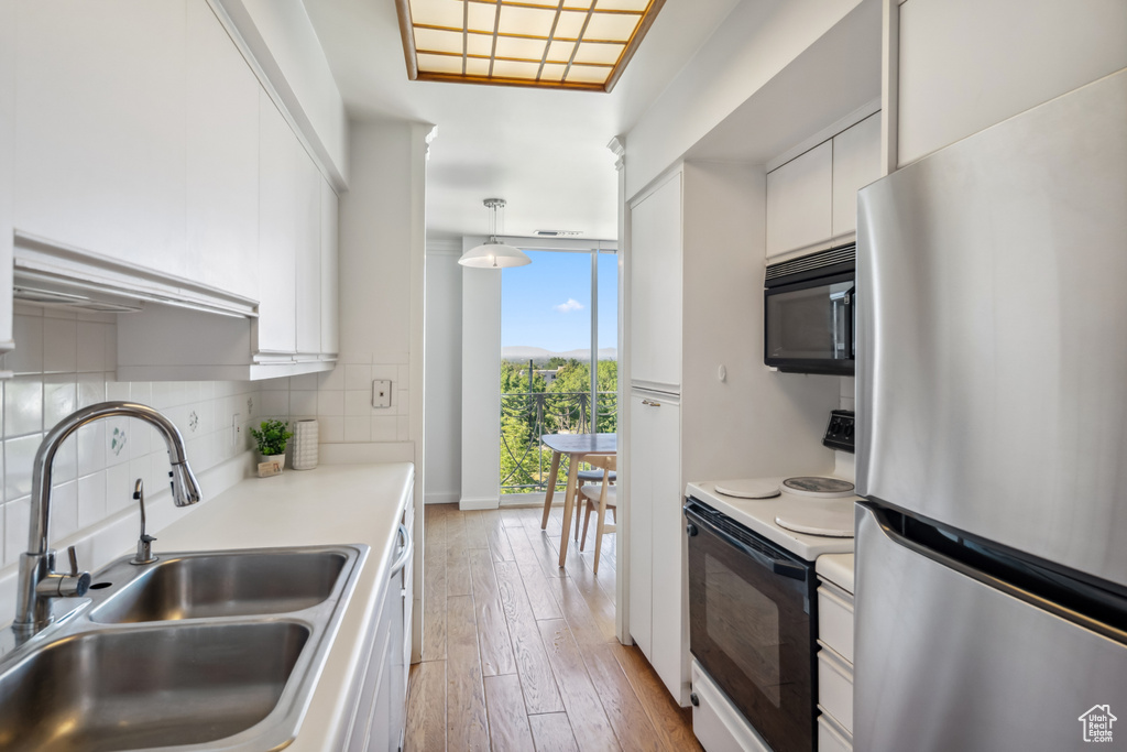 Kitchen featuring freestanding refrigerator, black microwave, electric range oven, light wood-style flooring, and white cabinetry