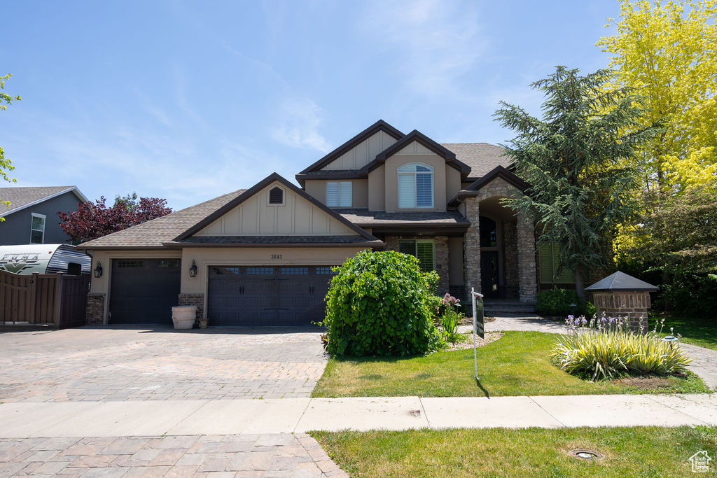 Craftsman-style home featuring an attached garage, driveway, stone siding, board and batten siding, and a shingled roof