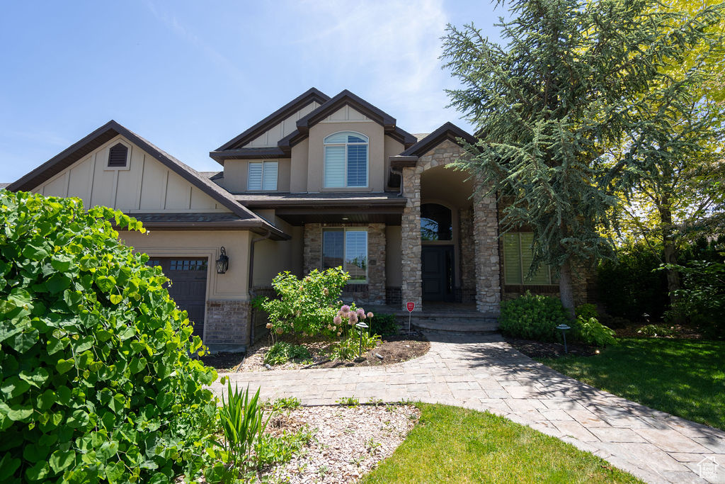 View of front of home featuring covered porch, stone siding, a garage, and stucco siding