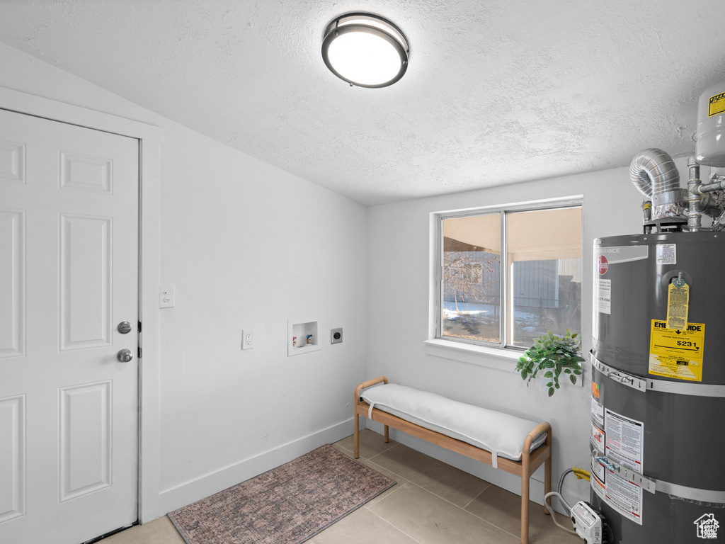 Clothes washing area featuring laundry area, strapped water heater, hookup for a washing machine, tile patterned flooring, and electric dryer hookup