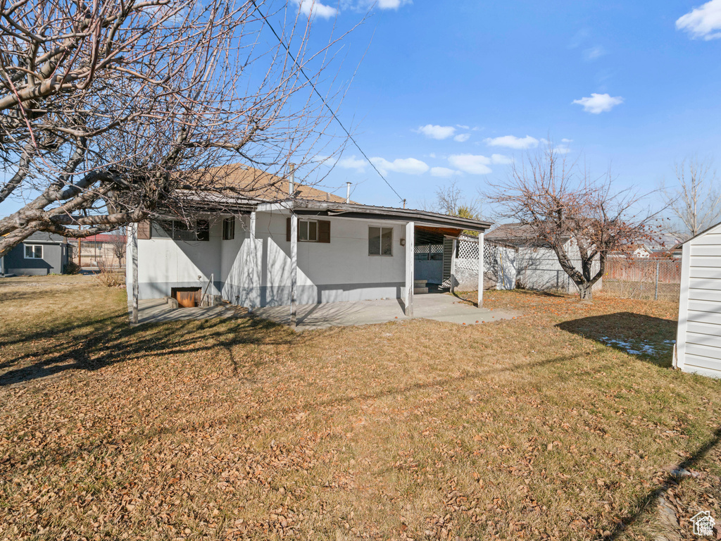 Rear view of property featuring roof with shingles, a lawn, a patio, and fence