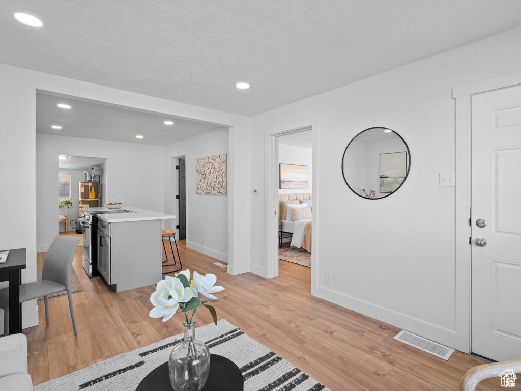 Living room with light wood finished floors, recessed lighting, visible vents, a textured ceiling, and baseboards