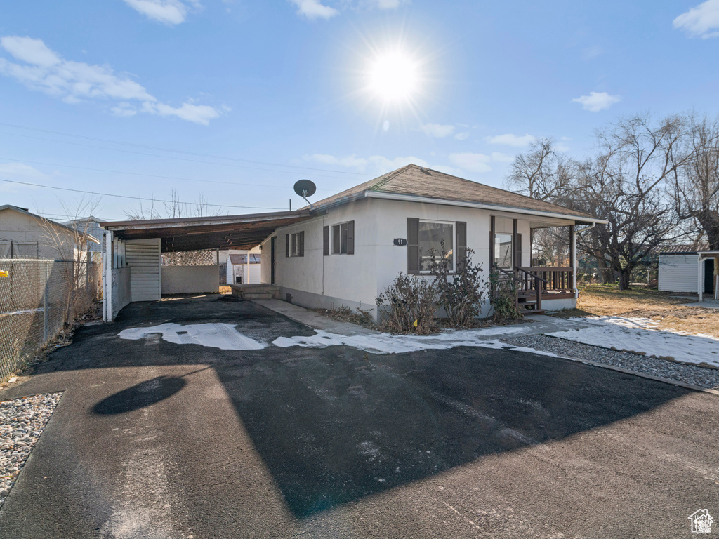 View of front of house with aphalt driveway, an attached carport, fence, and stucco siding