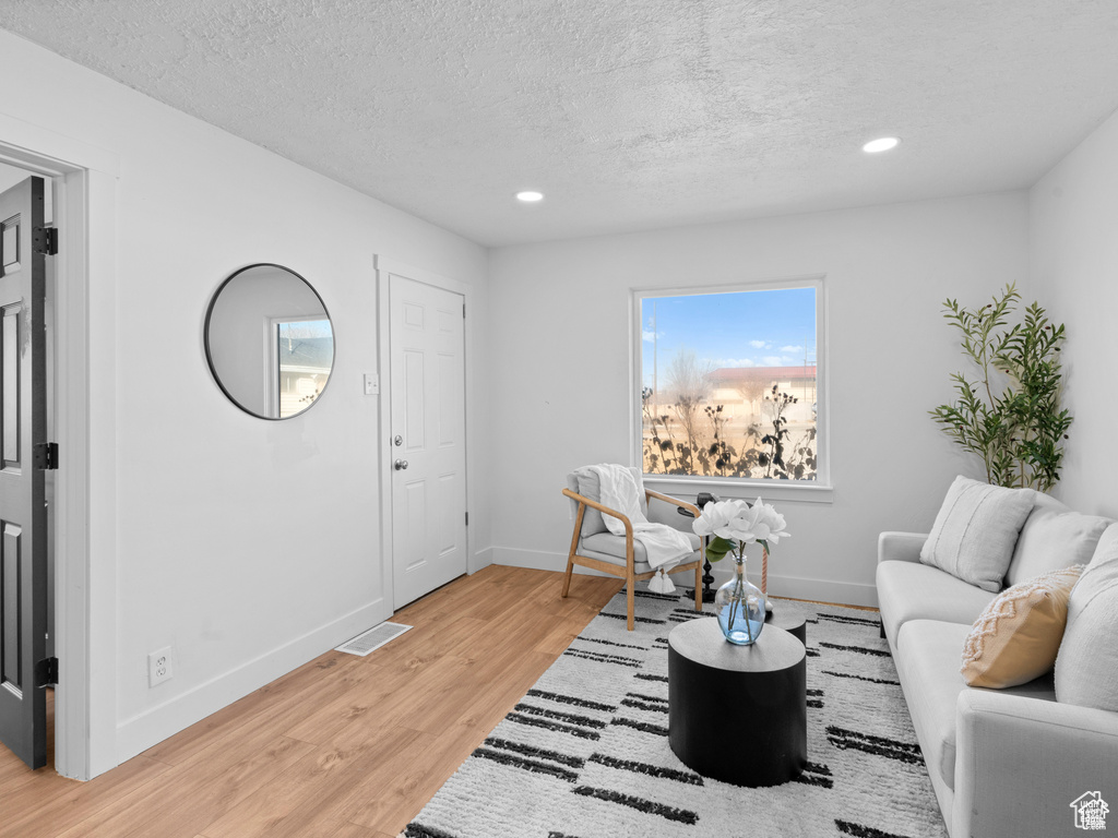 Living area featuring light wood-style flooring, a textured ceiling, visible vents, and baseboards