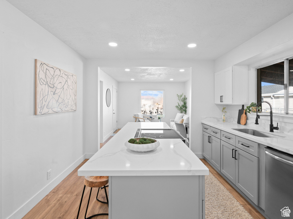 Kitchen featuring gray cabinetry, a kitchen island, a sink, light wood-type flooring, and dishwasher