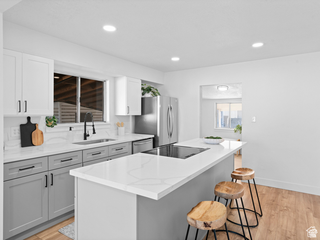 Kitchen featuring a kitchen island, appliances with stainless steel finishes, gray cabinetry, a kitchen bar, and a sink