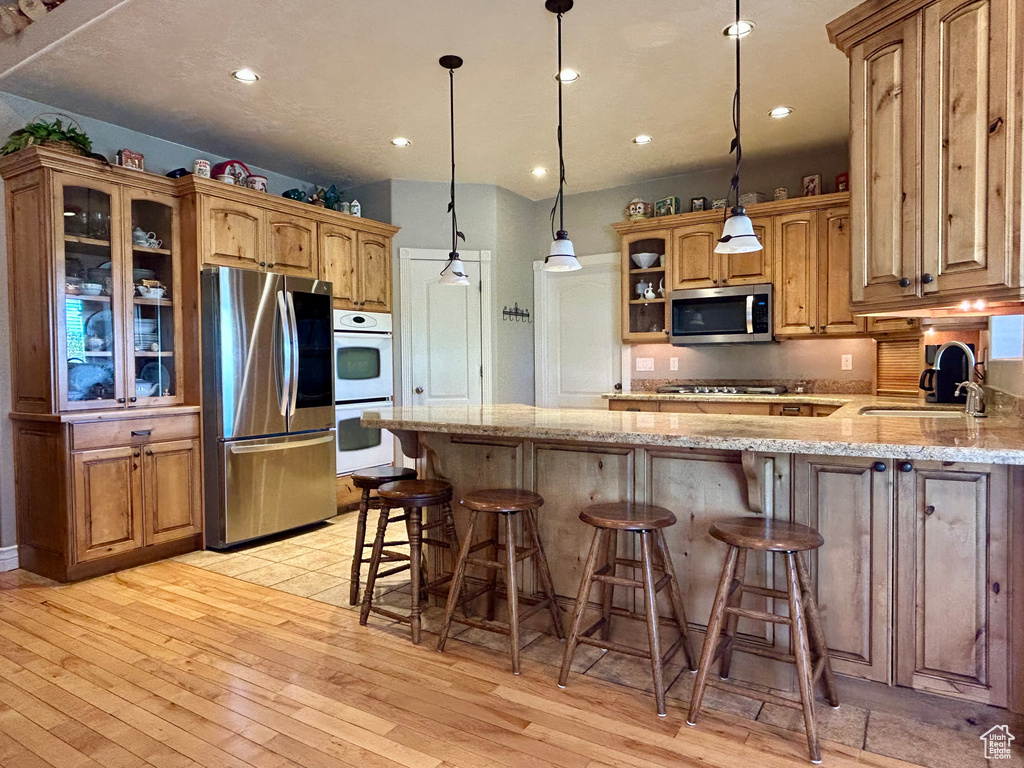 Kitchen with a sink, light wood-style flooring, stainless steel appliances, a peninsula, and glass insert cabinets