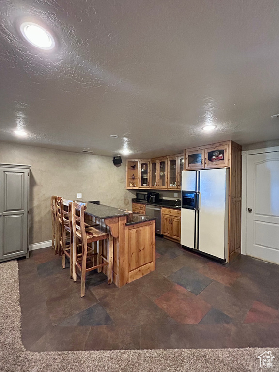 Kitchen featuring stainless steel dishwasher, a peninsula, a breakfast bar, glass insert cabinets, and white fridge with ice dispenser