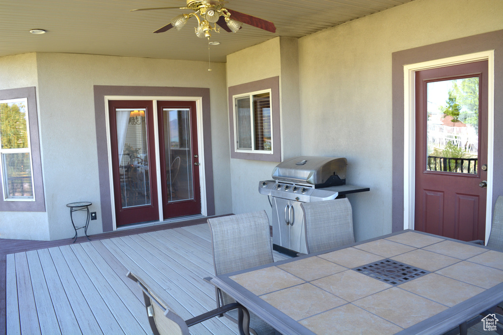 Wooden terrace featuring grilling area, ceiling fan, and outdoor dining space