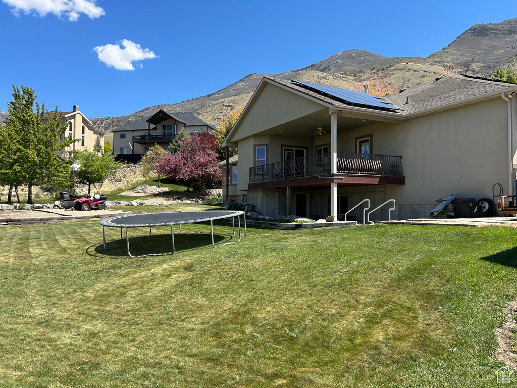 Back of house with solar panels, a trampoline, a lawn, a mountain view, and a balcony