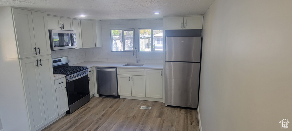 Kitchen featuring appliances with stainless steel finishes, a sink, a textured ceiling, backsplash, and white cabinetry