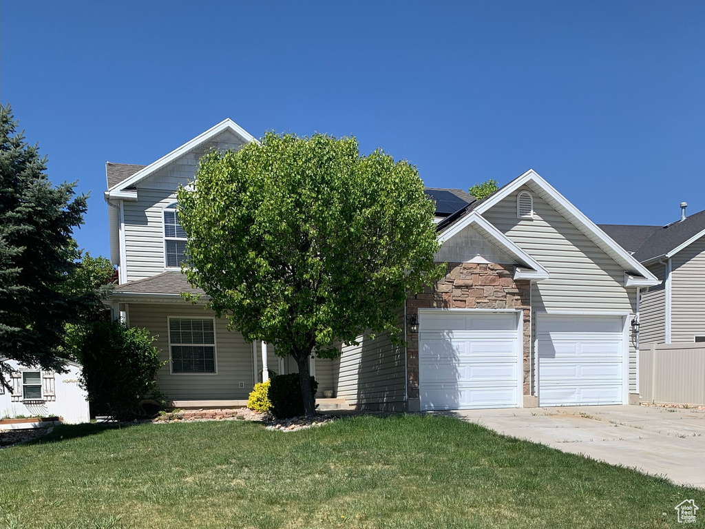 View of front of home with a garage, concrete driveway, a front yard, and solar panels