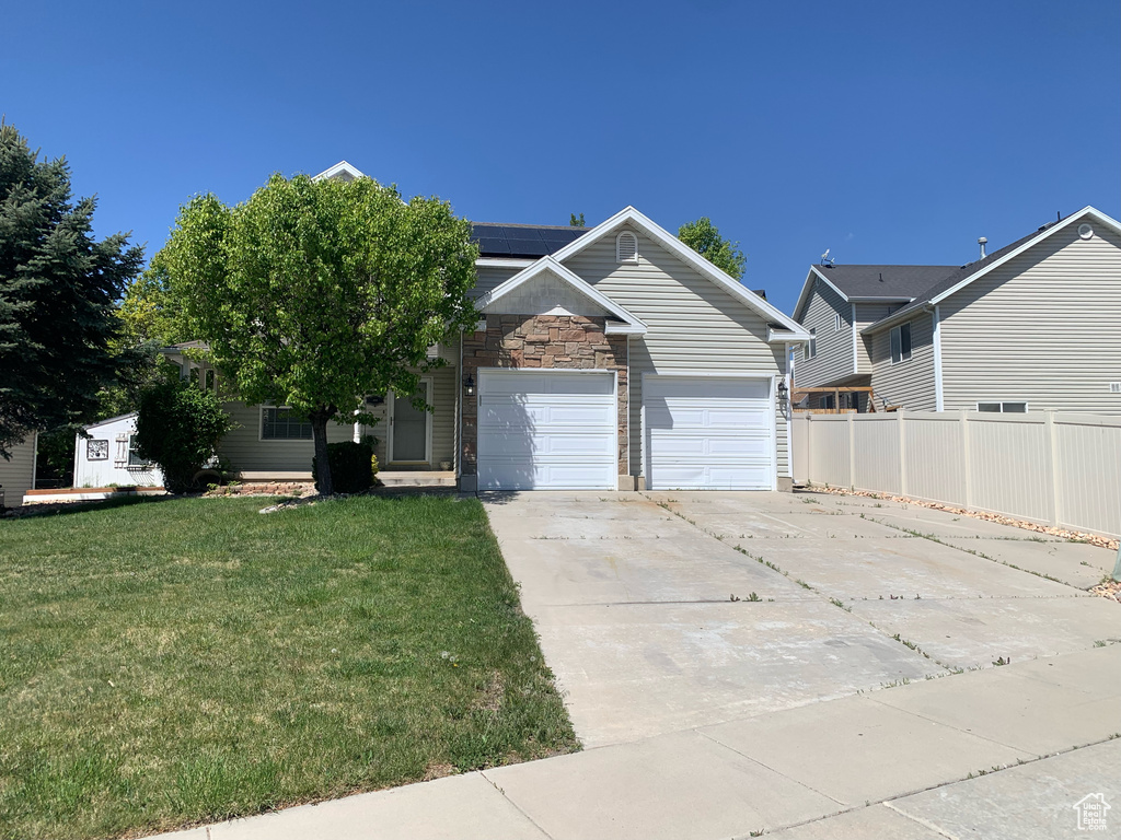 View of front of house with concrete driveway, solar panels, a garage, and stone siding