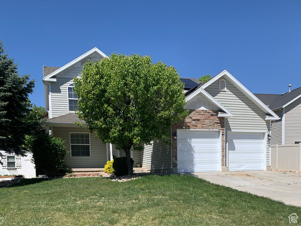 View of front of home with an attached garage, roof mounted solar panels, concrete driveway, and a front yard