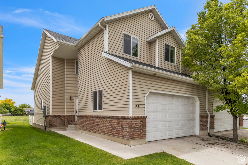 View of property exterior featuring brick siding, a garage, a lawn, and driveway
