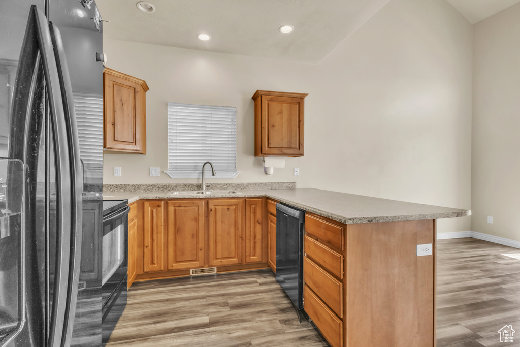 Kitchen with black appliances, a sink, a peninsula, light wood-style flooring, and recessed lighting