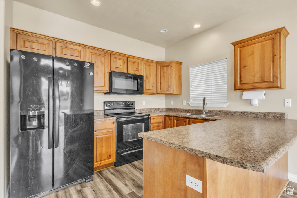Kitchen featuring black appliances, a sink, a peninsula, light wood-style flooring, and recessed lighting
