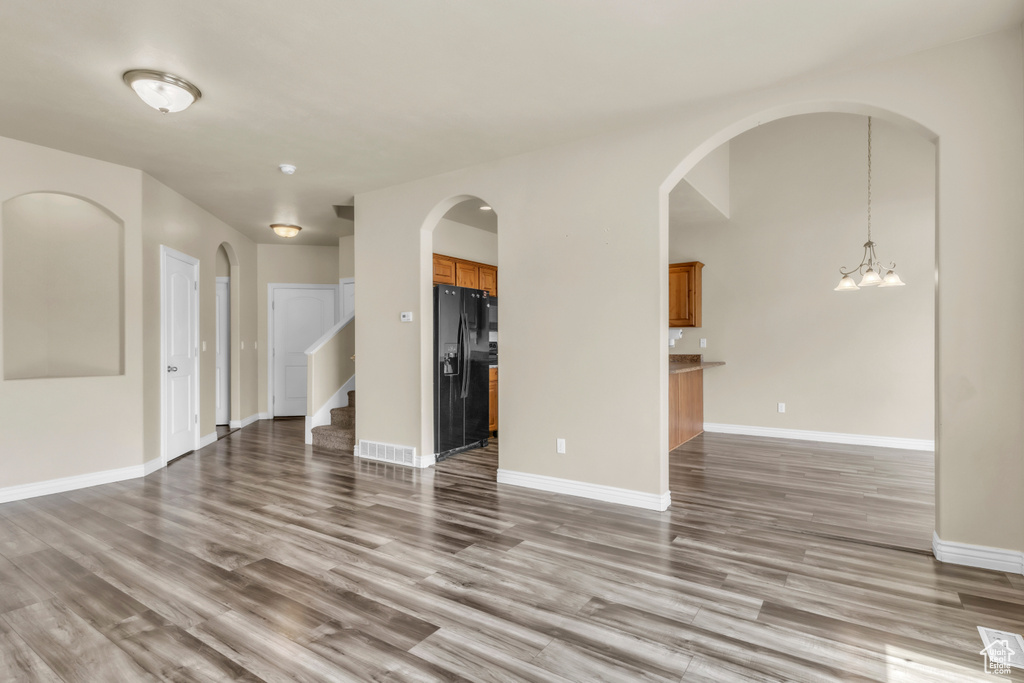 Unfurnished living room featuring wood finished floors, a chandelier, arched walkways, and stairs
