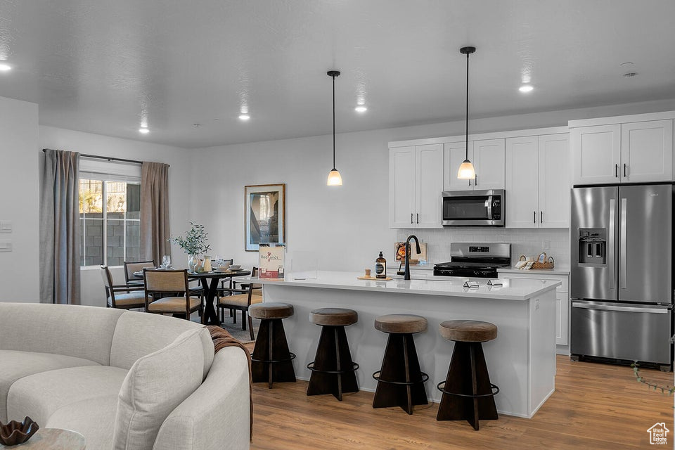 Kitchen with light wood-style flooring, appliances with stainless steel finishes, light countertops, white cabinetry, and backsplash