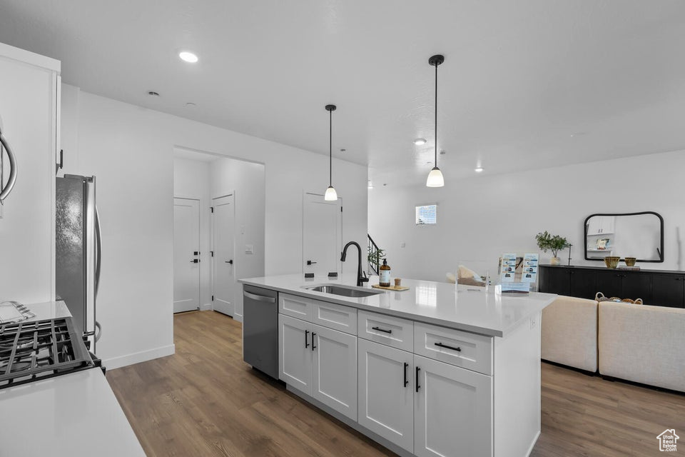 Kitchen featuring stainless steel appliances, open floor plan, white cabinets, a sink, and wood finished floors