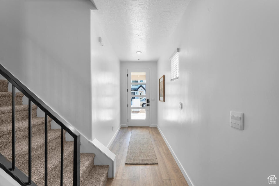 Doorway to outside featuring light wood-style floors, a textured ceiling, baseboards, and stairs
