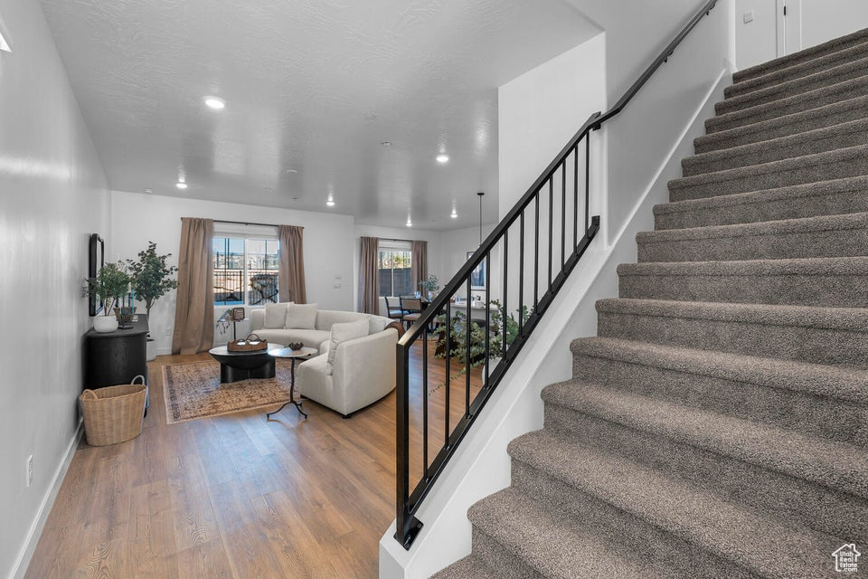 Stairs featuring a textured ceiling, baseboards, wood finished floors, and recessed lighting