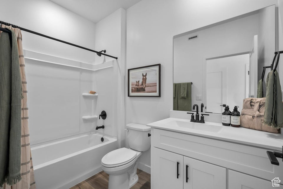 Full bath featuring toilet, wood finished floors, visible vents, vanity, and shower / bath combo