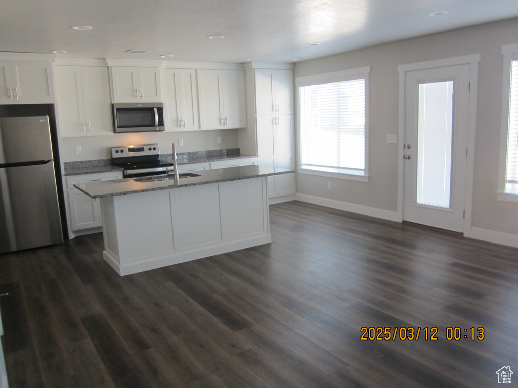 Kitchen with a center island with sink, stainless steel appliances, dark wood-style floors, and white cabinets