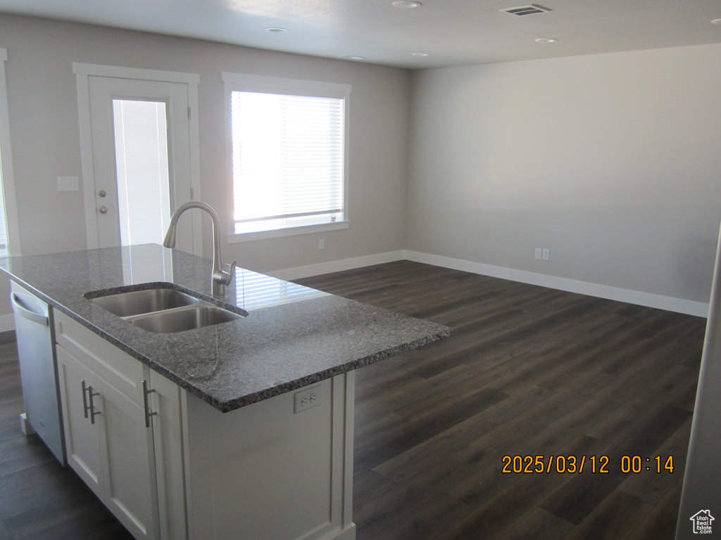 Kitchen featuring dark wood-style floors, baseboards, a center island with sink, a sink, and white cabinets