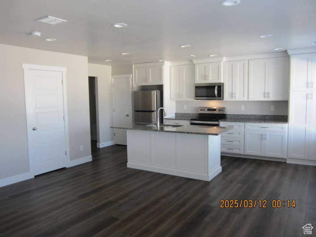 Kitchen with dark wood-type flooring, a center island with sink, a sink, white cabinetry, and stainless steel appliances