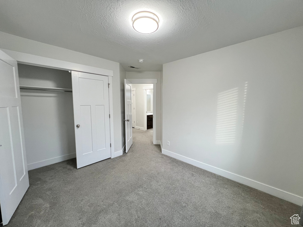 Unfurnished bedroom featuring a textured ceiling, a closet, carpet flooring, and baseboards