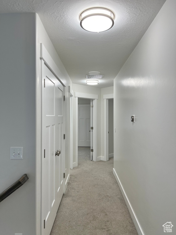 Corridor featuring a textured ceiling, baseboards, and light colored carpet