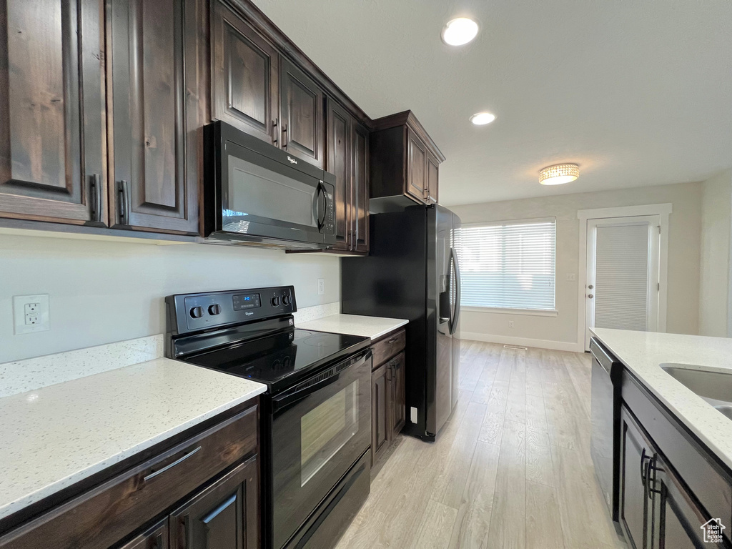 Kitchen with dark brown cabinetry, light wood-style floors, light stone counters, black appliances, and recessed lighting