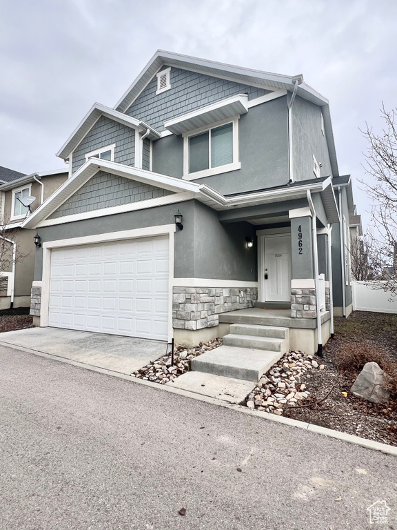View of front of home featuring stone siding, an attached garage, driveway, and stucco siding