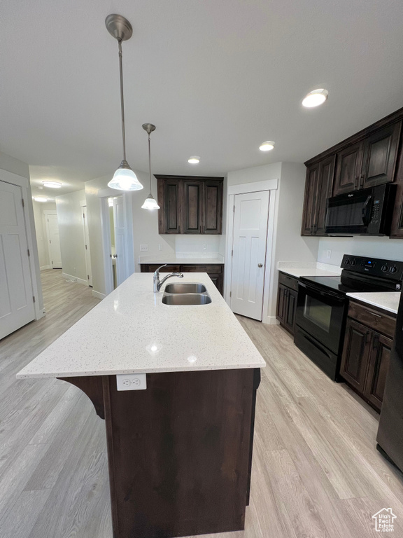 Kitchen with light wood finished floors, a kitchen island with sink, dark brown cabinetry, a sink, and black appliances
