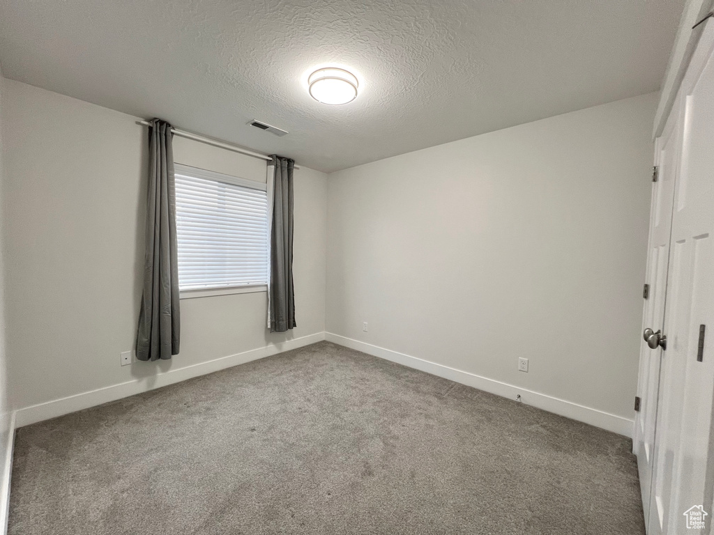 Spare room featuring a textured ceiling, carpet, visible vents, and baseboards