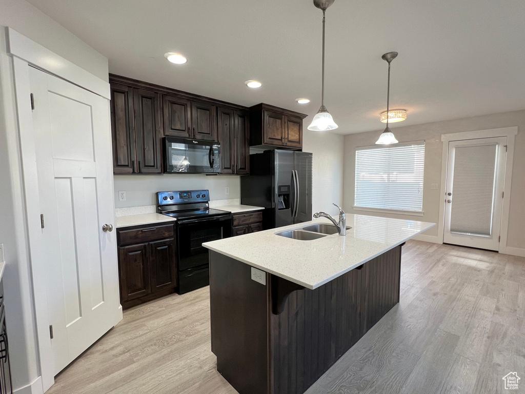 Kitchen with a center island with sink, light wood-style floors, dark brown cabinets, black appliances, and a sink