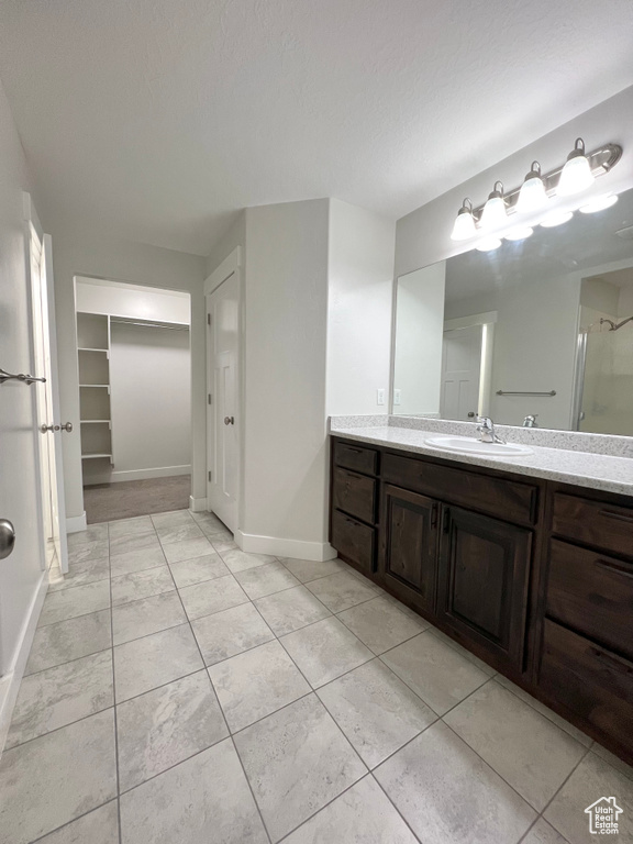 Full bathroom with a spacious closet, a textured ceiling, vanity, baseboards, and tile patterned floors