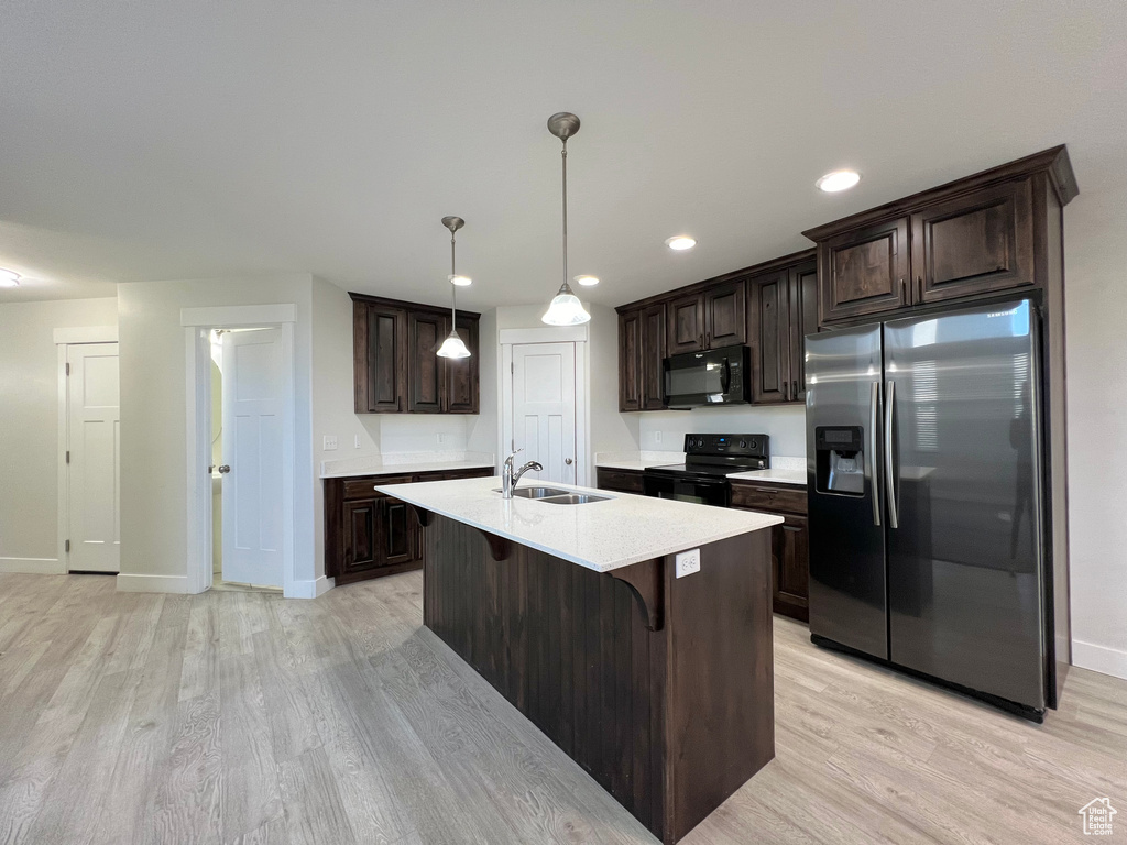 Kitchen with dark brown cabinetry, a breakfast bar, light countertops, black appliances, and a sink