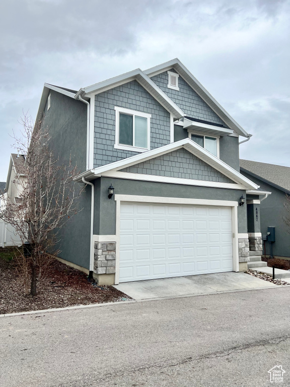 View of front of home with driveway, stone siding, a garage, and stucco siding