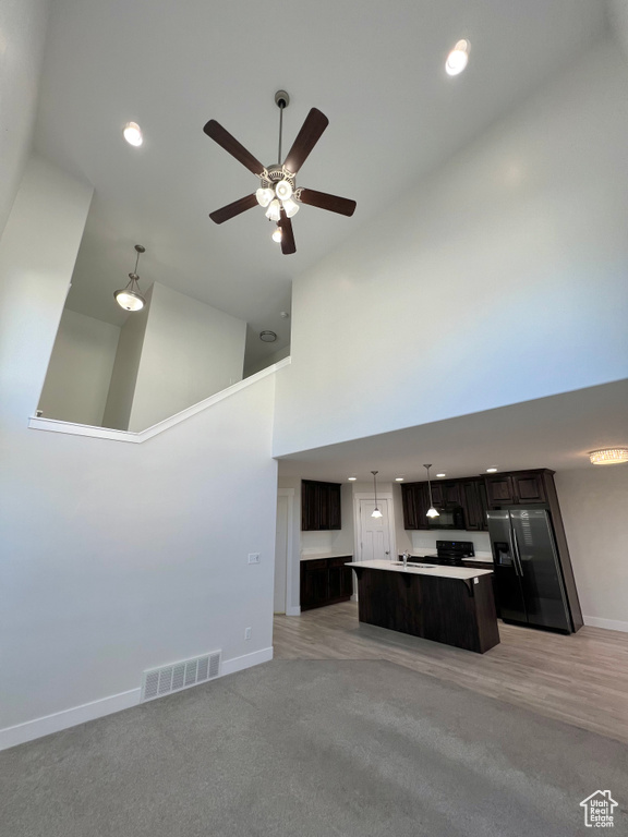 Kitchen with visible vents, a towering ceiling, open floor plan, a center island, and fridge with ice dispenser