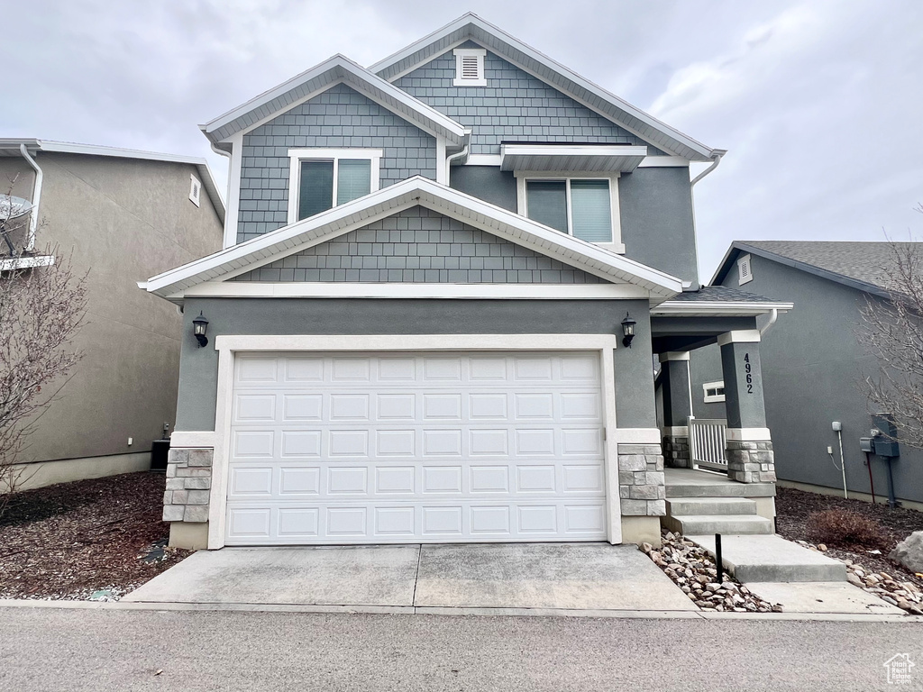 View of front of home featuring a garage, concrete driveway, stone siding, and stucco siding