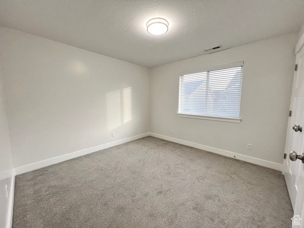 Spare room with a textured ceiling, carpet floors, visible vents, and baseboards