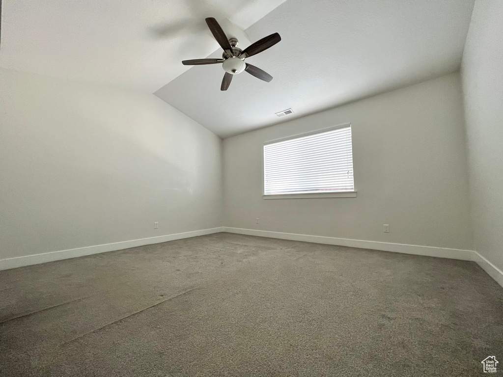 Unfurnished room featuring baseboards, visible vents, lofted ceiling, ceiling fan, and dark colored carpet