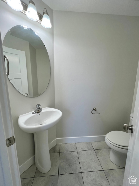 Half bathroom with baseboards, toilet, and tile patterned floors