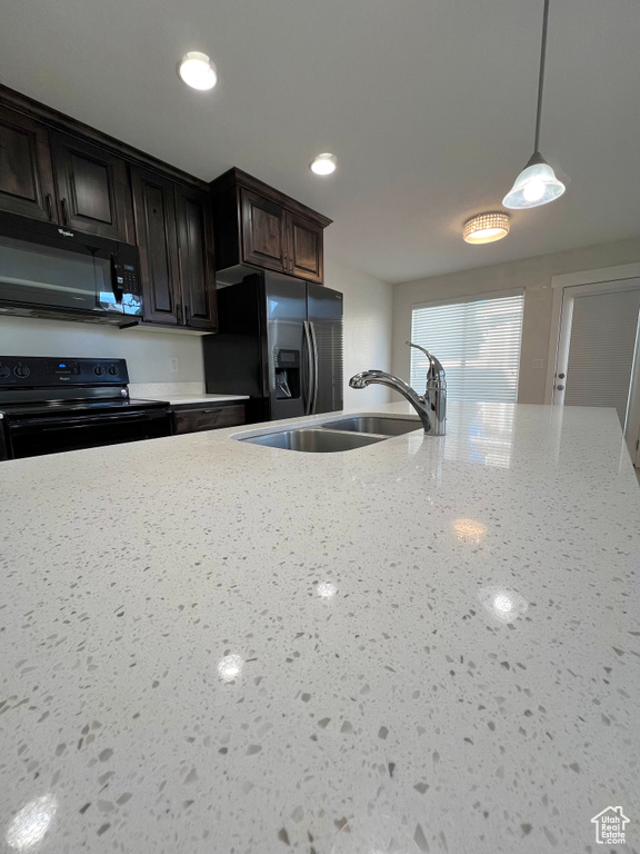 Kitchen featuring hanging light fixtures, light stone countertops, dark brown cabinets, black appliances, and a sink