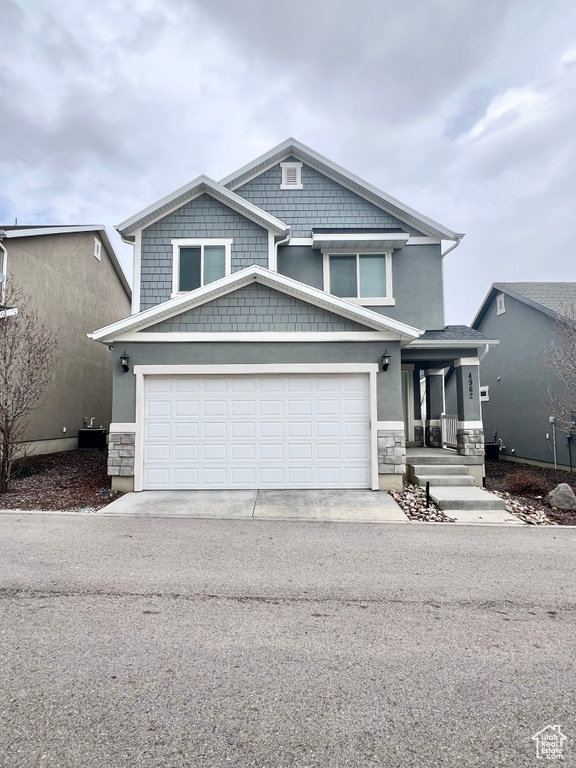 View of front facade featuring stone siding, driveway, and stucco siding
