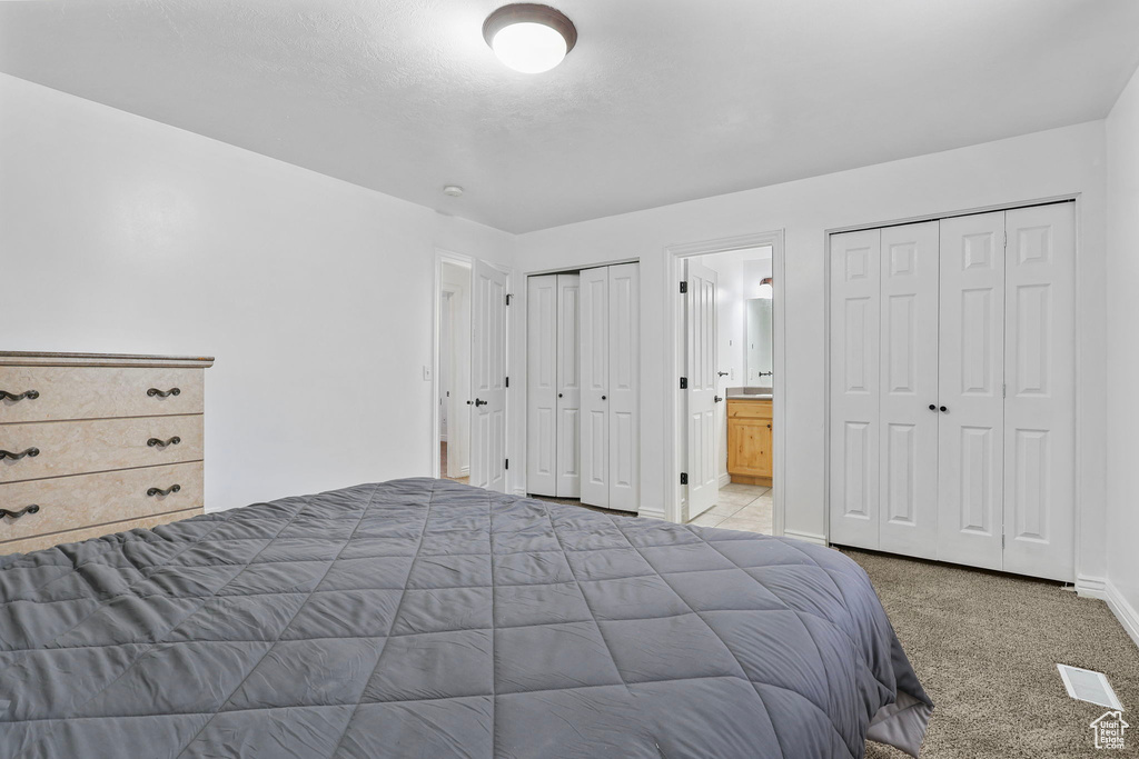 Carpeted bedroom with connected bathroom, baseboards, and two closets