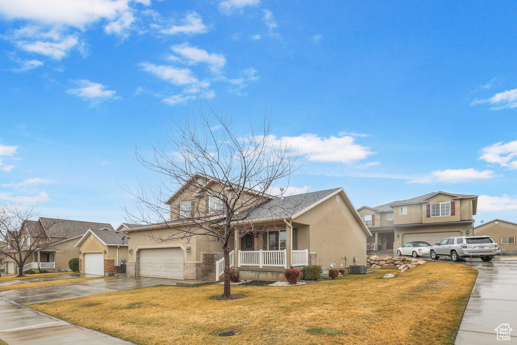 View of front facade featuring central AC unit, concrete driveway, stucco siding, a porch, and a front yard